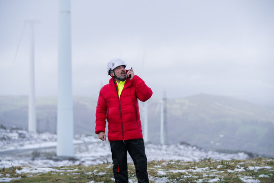 Engineer in red jacket using radio for maintenance at winter wind farm