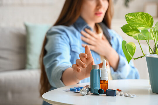 Young woman with asthma attack taking modern inhaler from coffee table in living room