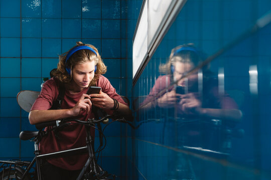 Teenager with bicycle and headphones using smartphone in urban setting