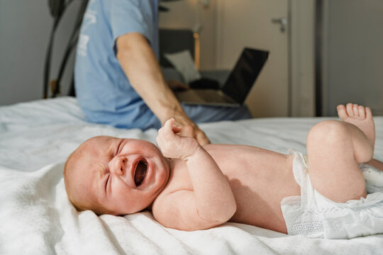 Crying newborn baby with father nearby in bedroom at home