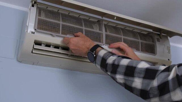 Male hands removing a dusty filter from a wall-mounted air conditioner for cleaning and maintenance