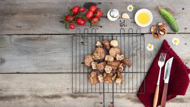 A grill with baked potatoes and zucchini was placed on an old wooden table. Cucumber, tomatoes, walnut, garlic clove, pepper, oil, and salt were on the table.