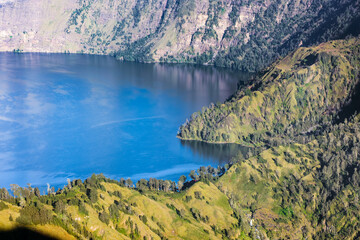 Fototapeta premium High angle view of Segara Anak lake surrounded by steep green crater walls of Mt Rinjani