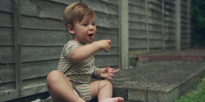 Young toddler sitting on the edge of a step in the backyard
