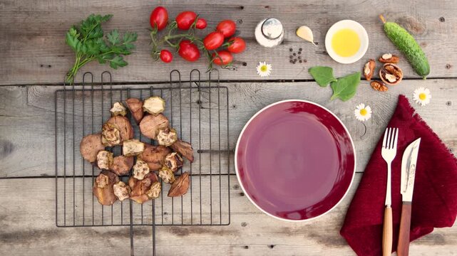 A grill with baked potatoes and zucchini was placed on an old wooden table. Cucumber, tomatoes, parsley, spinach, walnut, garlic clove, pepper, oil, and salt were on the table.