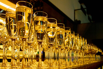 Many glasses of sparkling champagne lined up on a golden bar counter for a corporate banquet celebration. Professional luxury catering service for weddings and gala events with empty space for text. © Bondgofoto