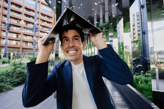 Smiling businessman using laptop for protection outdoors in modern city