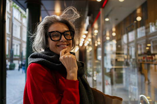 Smiling woman with gray hair and glasses outdoors in urban street
