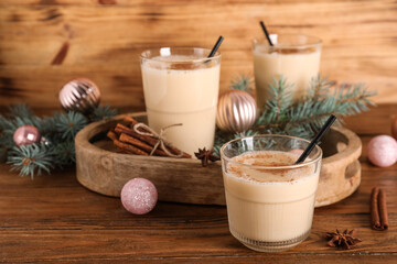 Glasses of tasty eggnog cocktail with cinnamon, fir branches and Christmas balls on wooden...