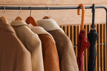 Rack with coats and umbrellas in room, closeup