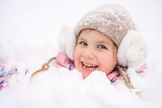 Smiling girl with earmuffs playing in snow during winter