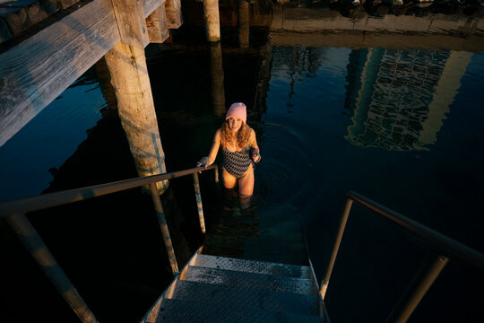 Smiling woman in swimwear taking an ice bath outdoors in winter lake