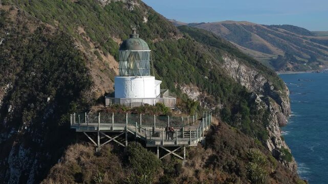 Tourists visiting Nugget Point lighthouse viewpoint on coastal cliffs in Otago New Zealand aerial view