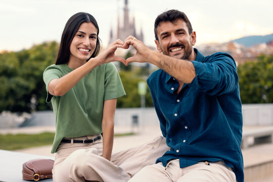 Smiling couple forming heart shape with hands outdoors in city park