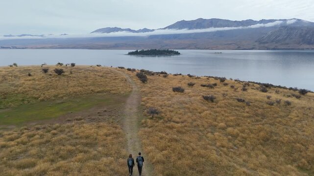 Aerial drone view of hikers walking trail above Lake Tekapo with mountains in Canterbury New Zealand