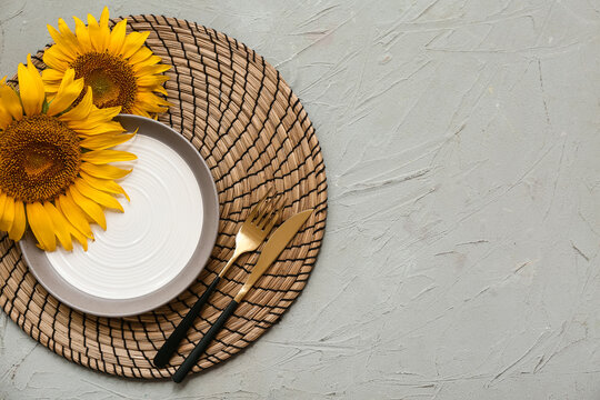 Beautiful table setting with golden cutlery and sunflowers on grey background