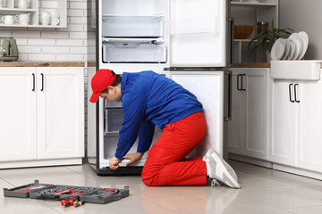 Male worker with tools repairing refrigerator in kitchen
