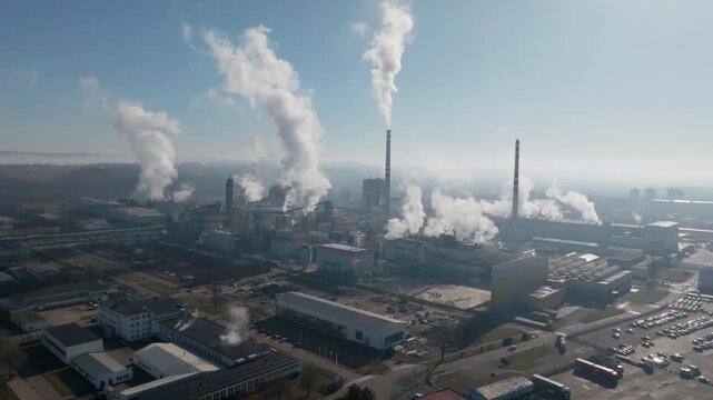 Drone shot along the riverside industrial area in &Scaron;tět&iacute;, with smokestacks emitting steam and mirrored reflections on calm water under bright sun.