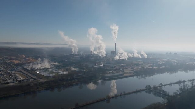 Drone shot showing the &Scaron;tět&iacute; industrial complex beside the river, with smokestacks venting steam and reflections visible on the calm water surface.