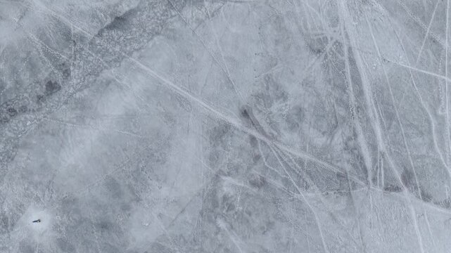 Drone video of a lone skater gliding on a vast, frozen lake. The surface is etched with patterns, creating a striking contrast against the serene winter landscape.