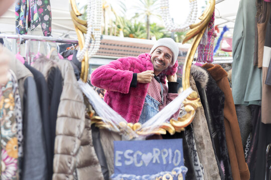 Customer at Barcelona flea market trying on fur coat smiling in mirror