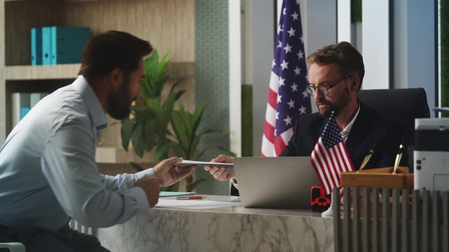 Middle-aged man applying for visa at U.S. embassy, handing document to official