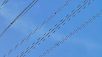 Utility wires forming a pattern against a clear blue sky, illustrating essential modern energy transmission infrastructure and power supply.
