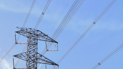 Tall steel lattice pylon carrying high voltage overhead power lines against a clear blue sky, symbolizing modern energy infrastructure and electricity transmission.