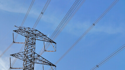 A robust industrial electricity pylon with multiple high-voltage power lines stands tall against a clear blue sky, symbolizing modern energy transmission infrastructure. © AmjadRosli