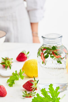 A jar with strawberry stems in a kitchen setting, surrounded by various fruits