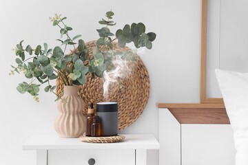 Air humidifier, essential oils and vase with eucalyptus branches on table in bedroom © Pixel-Shot
