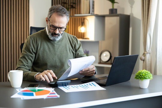 Man managing personal finances, reviewing documents, and using a calculator at his desk in a modern home office