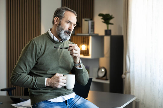 Thoughtful businessman with grey beard and green sweater pondering a new idea in a modern office, concentrating on solutions