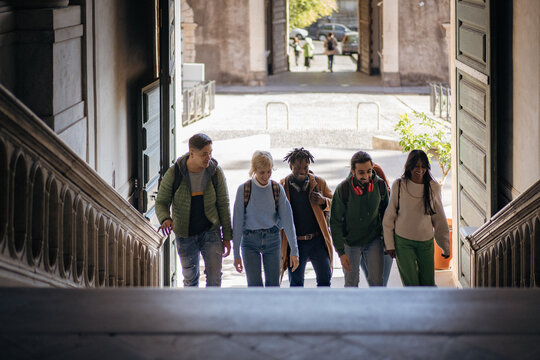 Diverse group of multi-ethnic students walking up stairs in a historic university building, smiling and talking during campus life