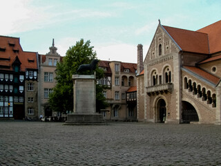 People sitting on the base of a lion statue in a town square.