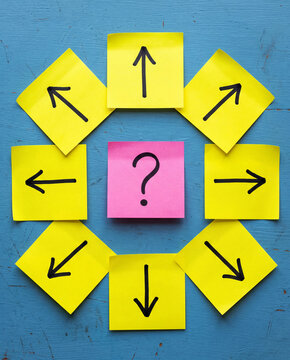 Question Mark on Pink Sticky Note Surrounded by Directional Arrows on Yellow Notes Over Blue Background, Decision Making and Choice Concept