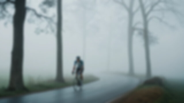 Blurred background of cyclist emerging from thick morning fog during World Bicycle Day ride, lone rider slowly appearing from mist on a quiet countryside road, soft silhouettes of trees fading.