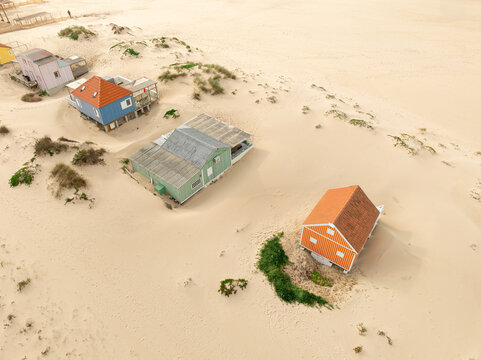 Costa da Caparica, Portugal - 18 December 2024: Aerial view of weathered beach houses amidst the golden sand dunes, their vibrant roofs punctuating the tranquil landscape.