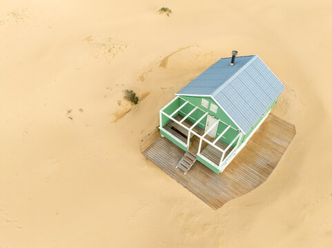 Costa da Caparica, Portugal - 06 March 2026: Aerial view of a lone green house standing out against a vast expanse of golden sand, a striking contrast of color and texture in this desolate landscape.