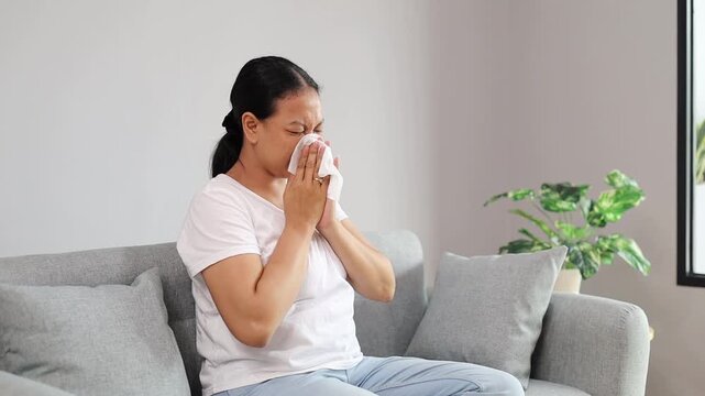 Asian Adult Woman sick with blowing nose sneezing with tissue for infection