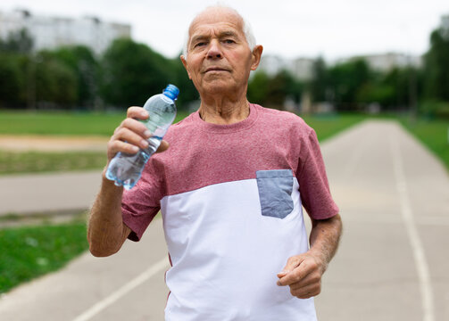 Old man with bottle of water running outdoors