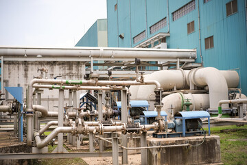 Industrial Plant with Intricate Network of Pipes Valves and Pumps Leading to a Large Blue Building Showcasing Complex Infrastructure and Energy Production Capabilities