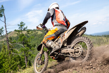 Close-up enduro rider on an dirt bike aggressively accelerating up rocky mountain slope, rear wheel...