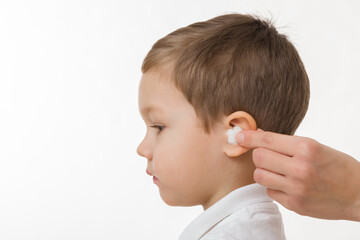 Young adult mother hand putting white soft cotton wool inside baby boy ear isolated on light gray background. Closeup. Ears pain. Side view.