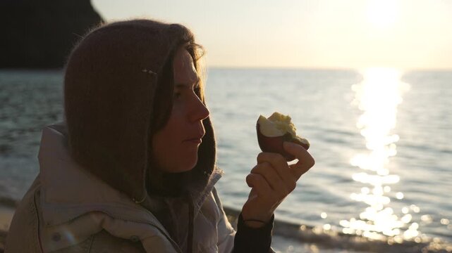 Woman eating baked sweet potato on a winter beach during beautiful golden sunset.