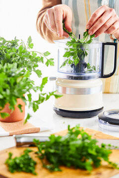 woman hands placing parsley into a food processor in a kitchen setting