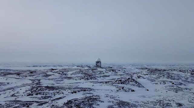 Cinematic aerial push toward a remote North Warning System radar dome in the snowy Arctic tundra near Iqaluit, showcasing isolated defense infrastructure in winter.