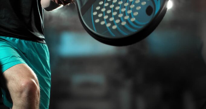 Super slow motion close-up of a padel player hitting a ball with a racket, filmed at 1000 fps. Dramatic studio lighting highlights the impact, motion and energy of the sport in a dynamic action. Speed