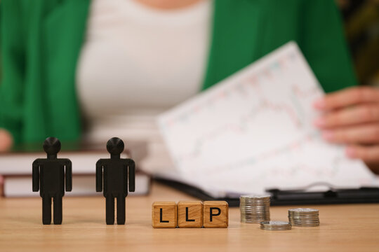 Two black figurines stand on a wooden table beside stacked coins and an LLP block. A person analyzes financial reports, exploring growth opportunities and partnership potential.