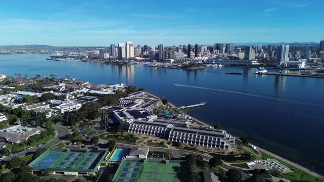 Bayfront skyline contrast frames Glorietta Bay Marina with downtown San Diego rising across water, speedboat movement. Smooth wakes, crisp tennis court geometry, reflective bay light, Coronado, CA